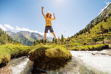 Glückliches Mädchen springt beim Wandern im Familienurlaub in Tirol in die Luft. Das Mädchen ist umgeben von der beeindruckenden Bergwelt in Tirol.