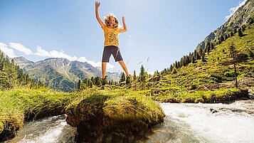 Glückliches Mädchen springt beim Wandern im Familienurlaub in Tirol in die Luft. Das Mädchen ist umgeben von der beeindruckenden Bergwelt in Tirol.