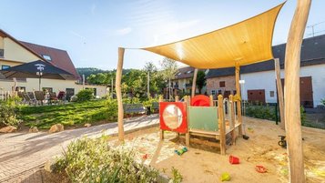 Sandspielplatz im Familienhotel Ottonenhof im Sauerland mit Sonnensegel, Spielgeräten und Sandspielzeug.