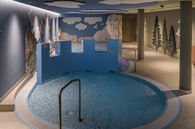 Kindgerechter Indoor-Wasserbereich im Zauchenseehof mit rundem Becken, spielerischer Burgwand und liebevoll gestalteter Naturkulisse an den Wänden.