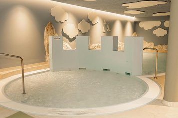 Kindgerechter Indoor-Wasserbereich mit 0,25m Tiefe im Zauchenseehof mit rundem Becken, spielerischer Burgwand und liebevoll gestalteter Naturkulisse an den Wänden.