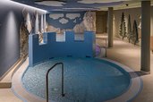Kindgerechter Indoor-Wasserbereich im Zauchenseehof mit rundem Becken, spielerischer Burgwand und liebevoll gestalteter Naturkulisse an den Wänden.