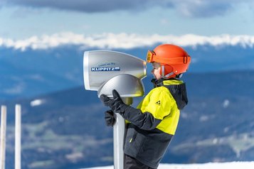 Junge blickt durch ein Fernrohr auf der Skipiste in Kärnten