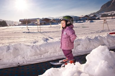 Ein Kind steht im Schnee auf dem Zauberteppich der Kinderskischule beim Familienhotel Landgut Furtherwirt in Tirol.