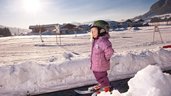 Ein Kind steht im Schnee auf dem Zauberteppich der Kinderskischule beim Familienhotel Landgut Furtherwirt in Tirol.