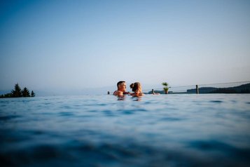Eltern genießen den Outdoor-Infinity-Pool mit Panoramablick im Familien Resort Petschnighof in Kärnten.
