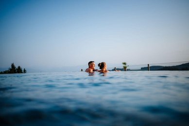Eltern genießen den Outdoor-Infinity-Pool mit Panoramablick im Familien Resort Petschnighof in Kärnten.