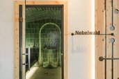 Dampfbad „Nebelwald“ im Zauchenseehof mit tiefgrünen, glänzenden Fliesen, gewölbter Nische und zentral platziertem Steinbehälter unter warmer Beleuchtung.