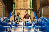 Zwei Kinder rutschen die Doppel-Indoor-Rutsche in der Spielanlage im Landhaus Averbeck in der Lüneburger Heide hinunter.