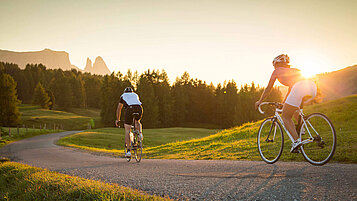  Ein Mann und einen Frau fahren zu Sonnenaufgang mit dem Fahrrad durch eine wunderschöne Landschaft in Südtirol
