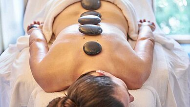 Eine Frau bekommt eine Massage mit heißen Steinen im Familienhotel Amiamo im Salzburger Land.