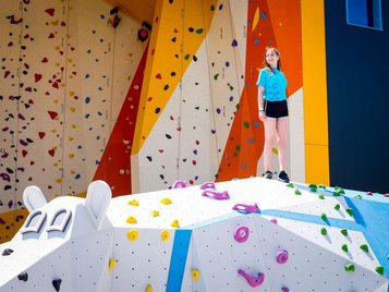 Ein Mädchen steht vor der riesigen Boulder- und Kletterwand im Bobo Fun Park im Kolping Family Resort in Ungarn.