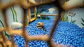 Kinder spielen in einem Bällebad mit blauen Bällen, das als Meeresszene gestaltet ist, mit Wandmalereien von Unterwasserleben im Spielbereich des Hotels Habachklause.