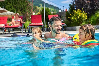 Kinder spielen mit ihrem Vater im Außenschwimmbad im Familienhotel Amiamo im Salzburger Land.