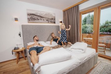 Familie entspannt im Familienzimmer des Familienhotel Furtherwirt, während das Kind fröhlich auf dem Bett spielt.