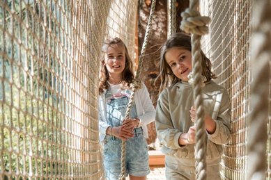 Zwei Mädchen gehen über einen Netzsteg im Waldspielbereich des Familienhotels Huber in Südtirol
