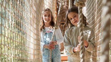 Zwei Mädchen gehen über einen Netzsteg im Waldspielbereich des Familienhotels Huber in Südtirol