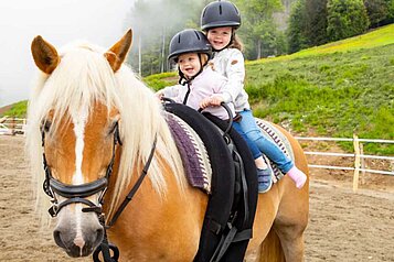 Zwei Kinder reiten auf einem Pony im Familienhotel Familien Resort Petschnighof in Kärnten.