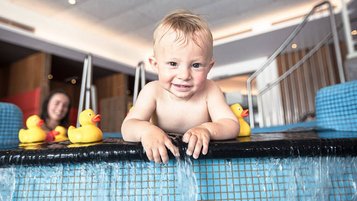 Ein kleiner Junge spielt und planscht in einem Indoorpool eines Familienhotels.