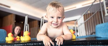 Ein kleiner Junge spielt und planscht in einem Indoorpool eines Familienhotels.
