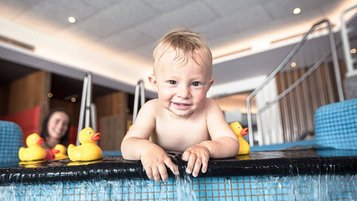 Ein kleiner Junge spielt und planscht in einem Indoorpool eines Familienhotels.