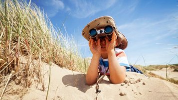 Junge liegt mit einem Fernglas in den Dünen mit Blick auf die Nordsee