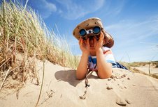 Junge liegt mit einem Fernglas in den Dünen mit Blick auf die Nordsee