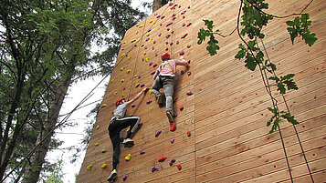 Zwei Jugendliche klettern eine Kletterwand in Südtirol nach oben.