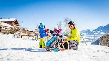 Eltern sitzen mit ihren beiden Kindern auf einem Schlitten im Schnee.