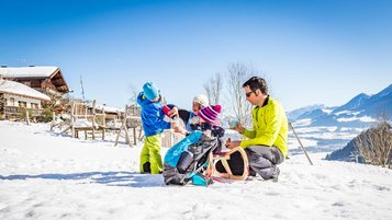 Eltern sitzen mit ihren beiden Kindern auf einem Schlitten im Schnee.