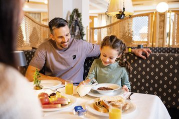 Vater und Tochter sitzen am Frühstückstisch im Familienhotel Alpenhotel Kindl in Tirol.