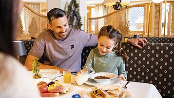 Vater und Tochter sitzen am Frühstückstisch im Familienhotel Alpenhotel Kindl in Tirol.