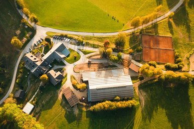 Luftaufnahme vom Familienhotel Ponyhof in Kärnten mit Reithalle, Tennisplätzen und umliegender Herbstlandschaft.