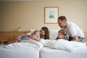 Familie mit zwei kleinen Kindern kuschelt gemeinsam im Zimmer des Familienhotel Sonne Bezau.