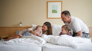 Familie mit zwei kleinen Kindern kuschelt gemeinsam im Zimmer des Familienhotel Sonne Bezau.