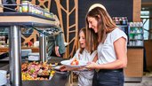 Mutter und Tochter bedienen sich am Buffet im Restaurant des Familienhotels Aigo welcome family in Oberösterreich