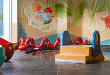 Bunter Indoor-Wasserbereich mit kleinem Becken, Mini-Rutsche, roten Wasserschlangen und verspieltem Wandbild für Kleinkinder im Familienhotel Amiamo.