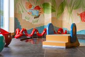 Bunter Indoor-Wasserbereich mit kleinem Becken, Mini-Rutsche, roten Wasserschlangen und verspieltem Wandbild für Kleinkinder im Familienhotel Amiamo.