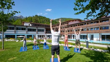 Zusammen mit einem Trainer machen Erwachsene und Kinder Bewegungsübungen im Garten des Familienhotel Das Bayrischzell in Oberbayern