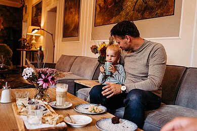 Vater und Sohn sitzen mit Kuchen und Kaffee in der gemütlichen Lounge des Familienhotels Landhaus Averbeck in der Lüneburger Heide.