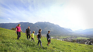 Familie mit drei Kindern wandert über eine Wiese im Familienurlaub Liechtenstein.