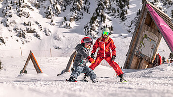 Winter im Salzburger Land: Kind lernt in der Kinderskischule mit einem Skilehrer das Skifahren