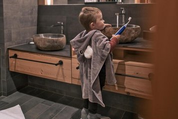 Ein Kind steht mit einem Handtuch im Badezimmer eines Zimmers im Familienhotel Gorfion in Liechtenstein.