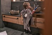 Ein Kind steht mit einem Handtuch im Badezimmer eines Zimmers im Familienhotel Gorfion in Liechtenstein.