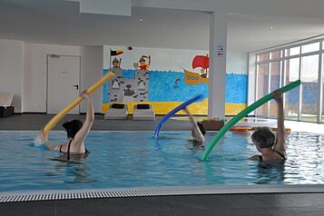 Drei Frauen beim Aquagym mit Schwimmnudeln im Schwimmbad des Familienhotels Gut Landegge im Emsland.