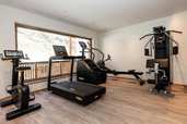 Fitnessraum im Familienhotel Oberkarteis im Salzburger Land mit Laufband, Trainingsgeräten und Aussicht nach draußen.