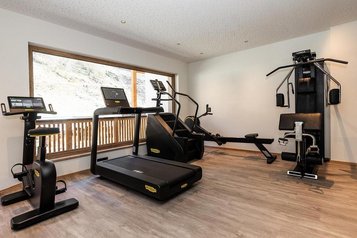 Fitnessraum im Familienhotel Oberkarteis im Salzburger Land mit Laufband, Trainingsgeräten und Aussicht nach draußen.