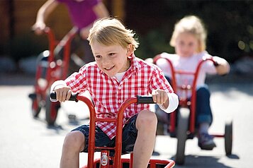 Glückliche Kinder fahren auf dem Dreirad auf dem Außengelände des Familienhotels Sonnenpark.