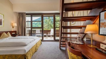 Familienzimmer im Hotel Sonngastein im Salzburger Land mit Doppelbett, Holztreppe, Schreibtisch und Balkonblick.
