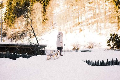 Durch die verschneite Winterlandschaft zieht ein Kind seinen Schlitten beim Familienhotel Alpura Retreat in Südtirol.